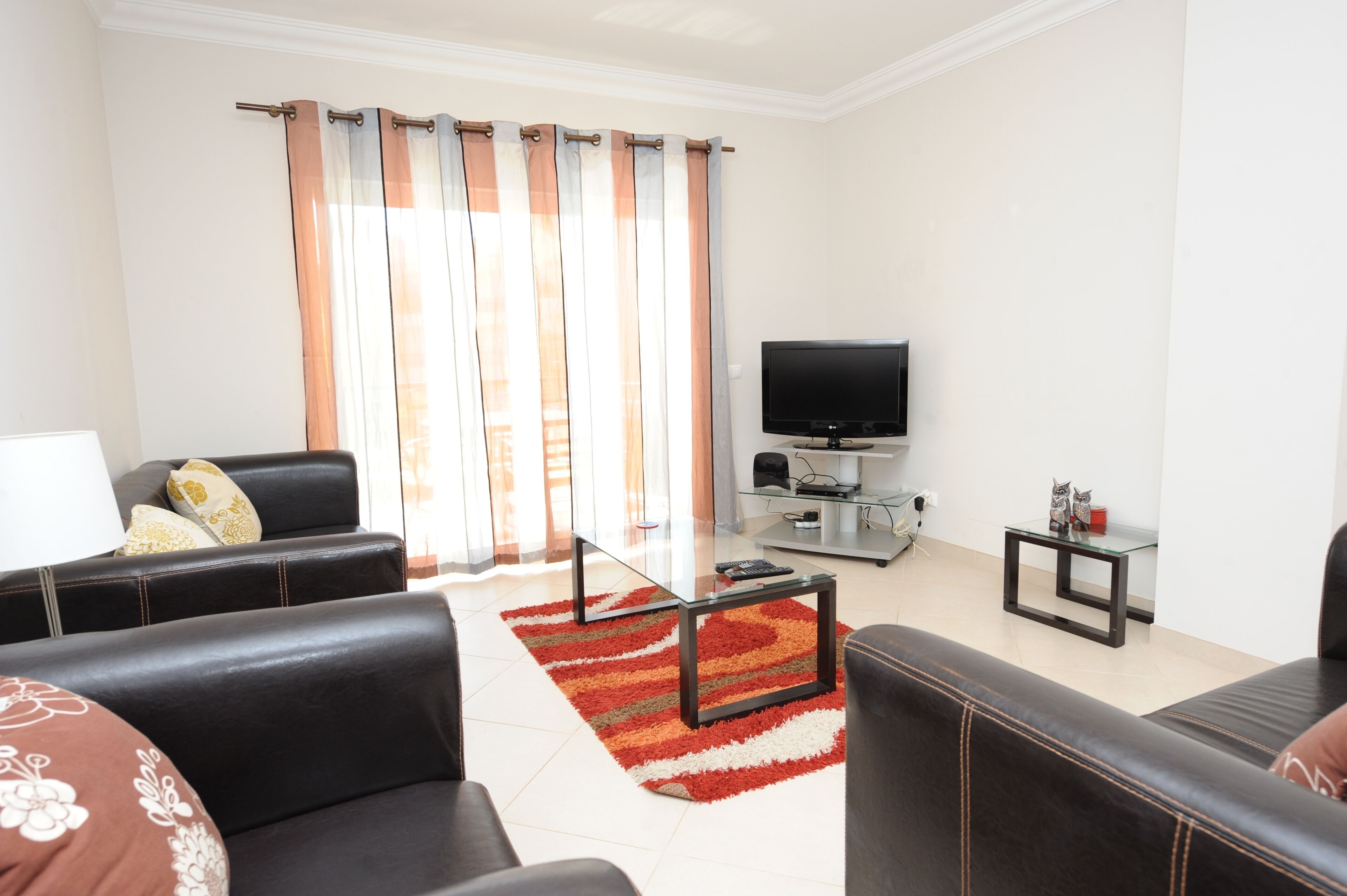 A modern living room with leather sofas, a glass coffee table, a flat-screen TV, and a striped rug.
