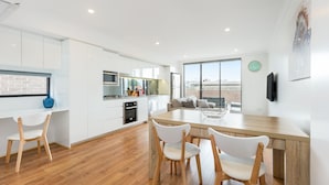 A modern kitchen with white cabinets, a wooden dining table, and a large window overlooking a cityscape. - Balmain Modern Apartments (Rozelle)