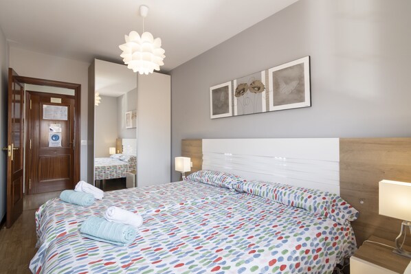 A hotel room with a large bed, a wooden headboard, a bedside table with a lamp, and a mirror on the wall. - Apartment next to the Plaza Mayor, Wifi and Parking - leonapartamentos (León)