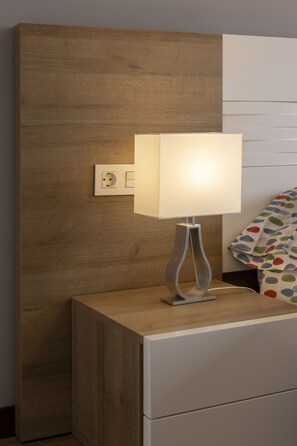 A bedside table with a lamp, a power outlet, and a bed with a colorful pillow. - Apartment next to the Plaza Mayor, Wifi and Parking - leonapartamentos (León)