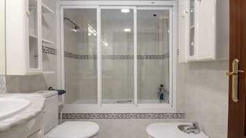 Un baño con dos inodoros, una cabina de ducha y un lavabo.
