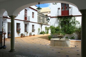 An open courtyard with a fountain, potted plants, and white buildings with red window frames and balconies. - 1 bedroom, private terrace (Sevilla)