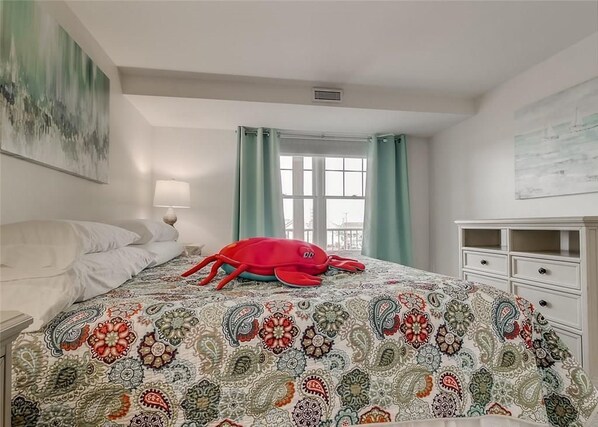 Un dormitorio con una cama, una mesita de noche, una lámpara, una ventana con cortinas y un cuadro en la pared.