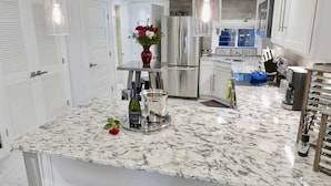 A modern kitchen with a marble countertop, stainless steel appliances, and a vase with flowers.