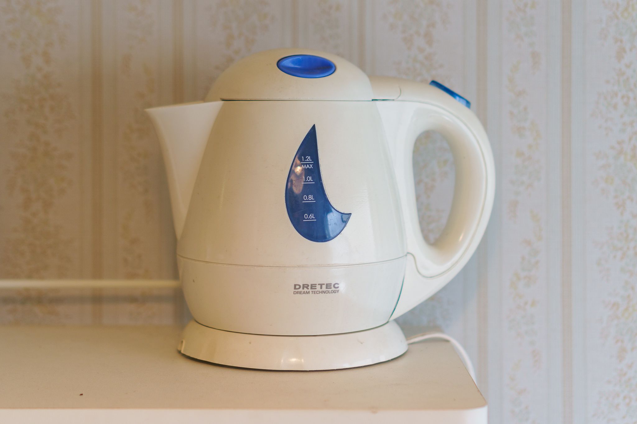 A white electric kettle with a blue control panel and a handle, placed on a white countertop.