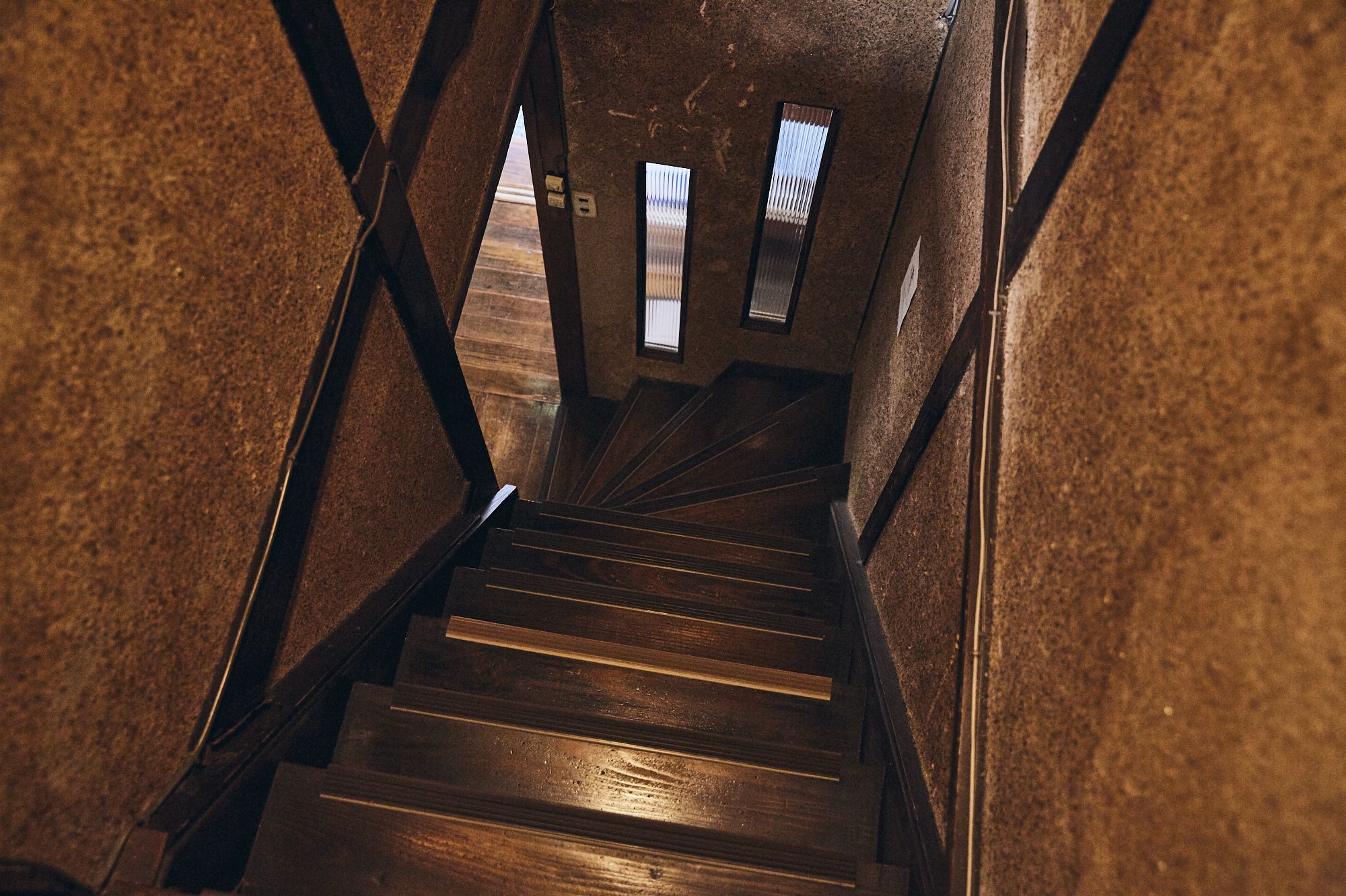 A wooden staircase with metal railings and a view of the upper floor through a window.