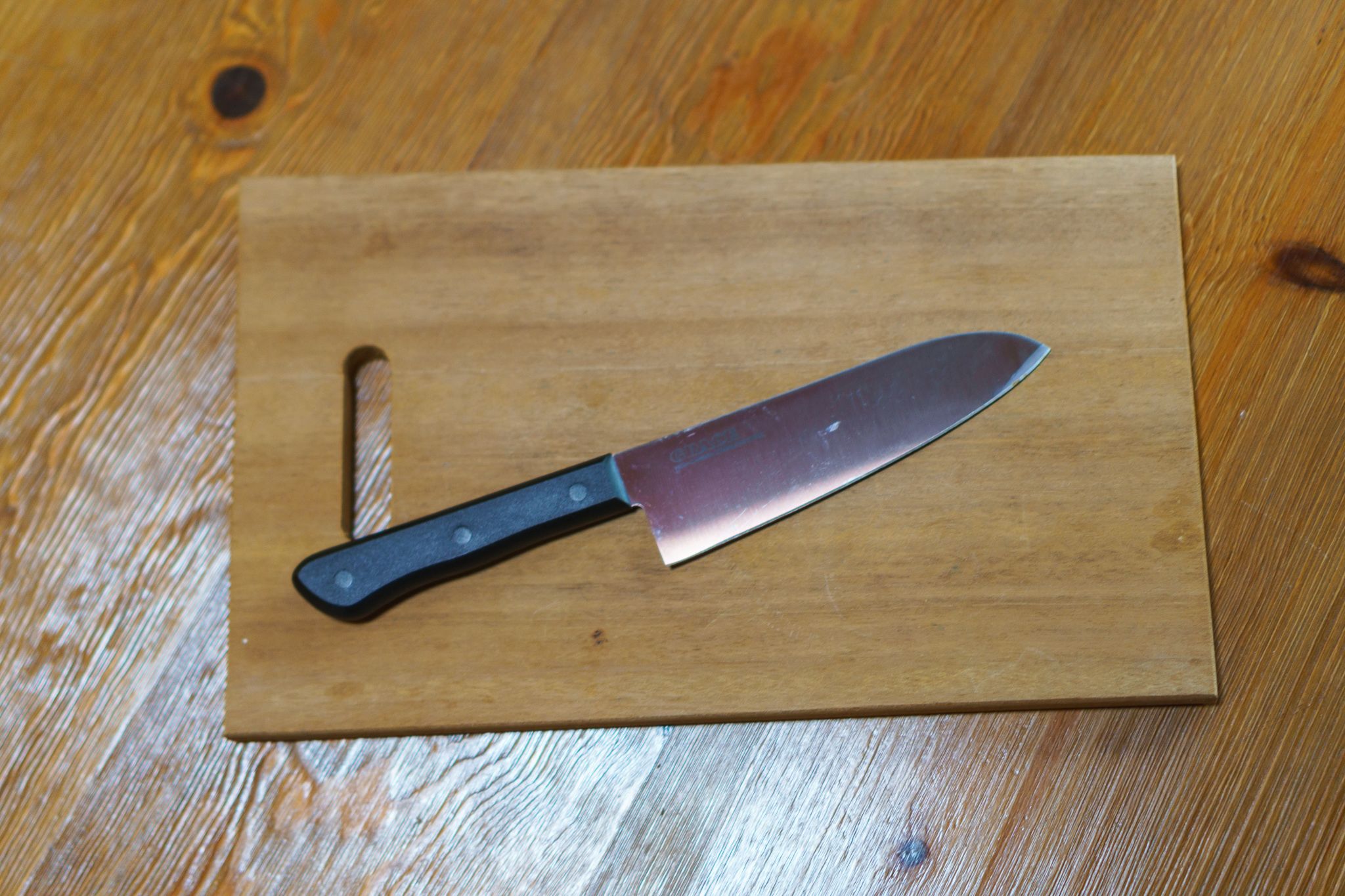 Un cuchillo con mango negro sobre tabla de madera.