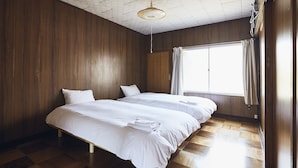 Una habitación con dos camas, paredes de madera, una ventana con cortinas y una lámpara colgante.