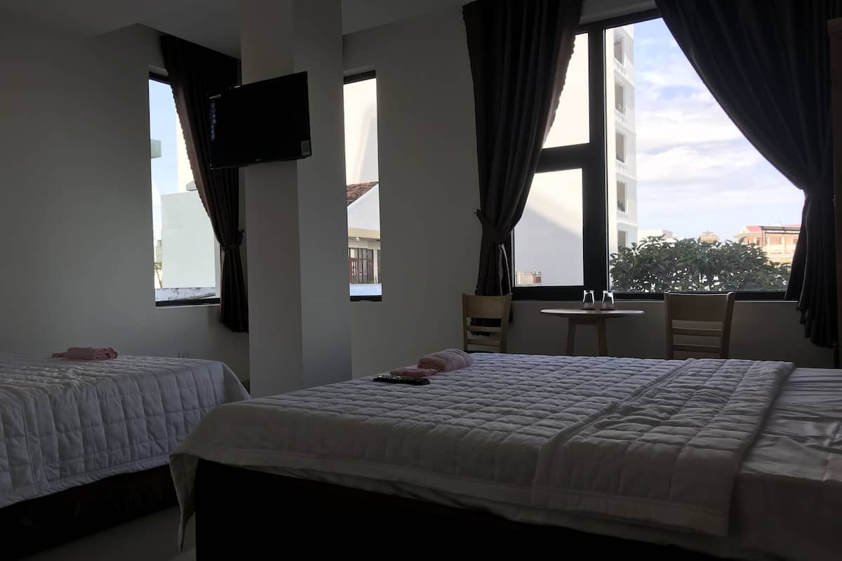 Quarto de hotel com duas camas, televisão presa à parede, uma mesa pequena e uma cadeira.