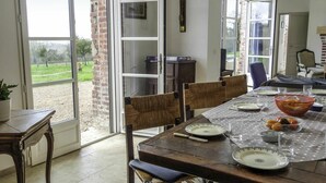 A dining area with a table set for four, surrounded by wicker chairs, a wooden bench, and a potted plant.