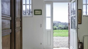 A hallway with a wooden door, a white door leading to a garden, and a framed picture on the wall.