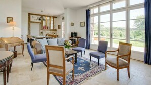 A spacious living room with a large window, a dining area, and a kitchen in the background.