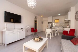 A modern living room with a flat-screen TV, a white coffee table, red chairs, and a grey sofa.