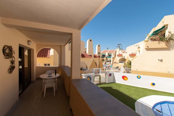 A balcony with a table and chairs, a view of a pool area, and a building with a distinctive architectural style.