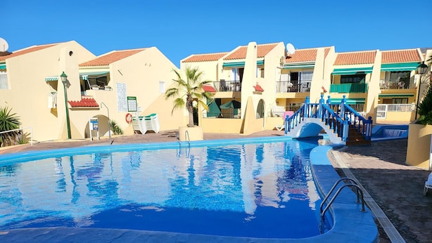 A swimming pool with a blue edge, surrounded by buildings with red-tiled roofs and balconies. - Mare Verde 1 (Costa Adeje)