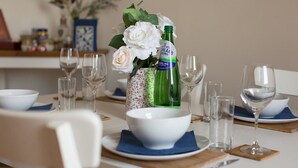 A dining table set with white bowls, napkins, and wine glasses, with a bottle of Highland Spring Sparkling water and a vase of white flowers.