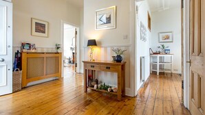 A hallway with wooden flooring, a wooden console table with a lamp, and a white shelving unit.