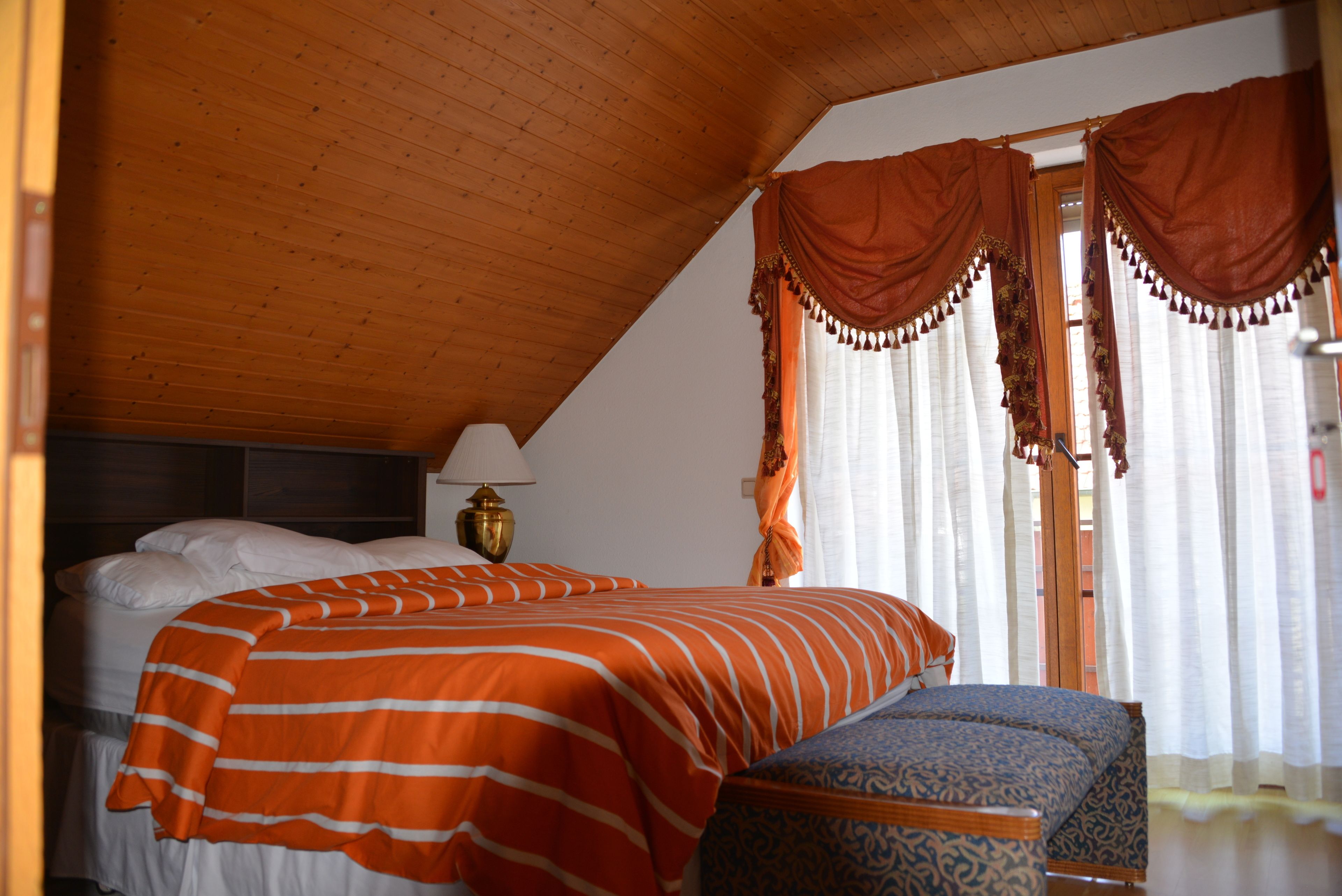 Un dormitorio con cama, mesita de noche, lámpara y ventana con cortinas.