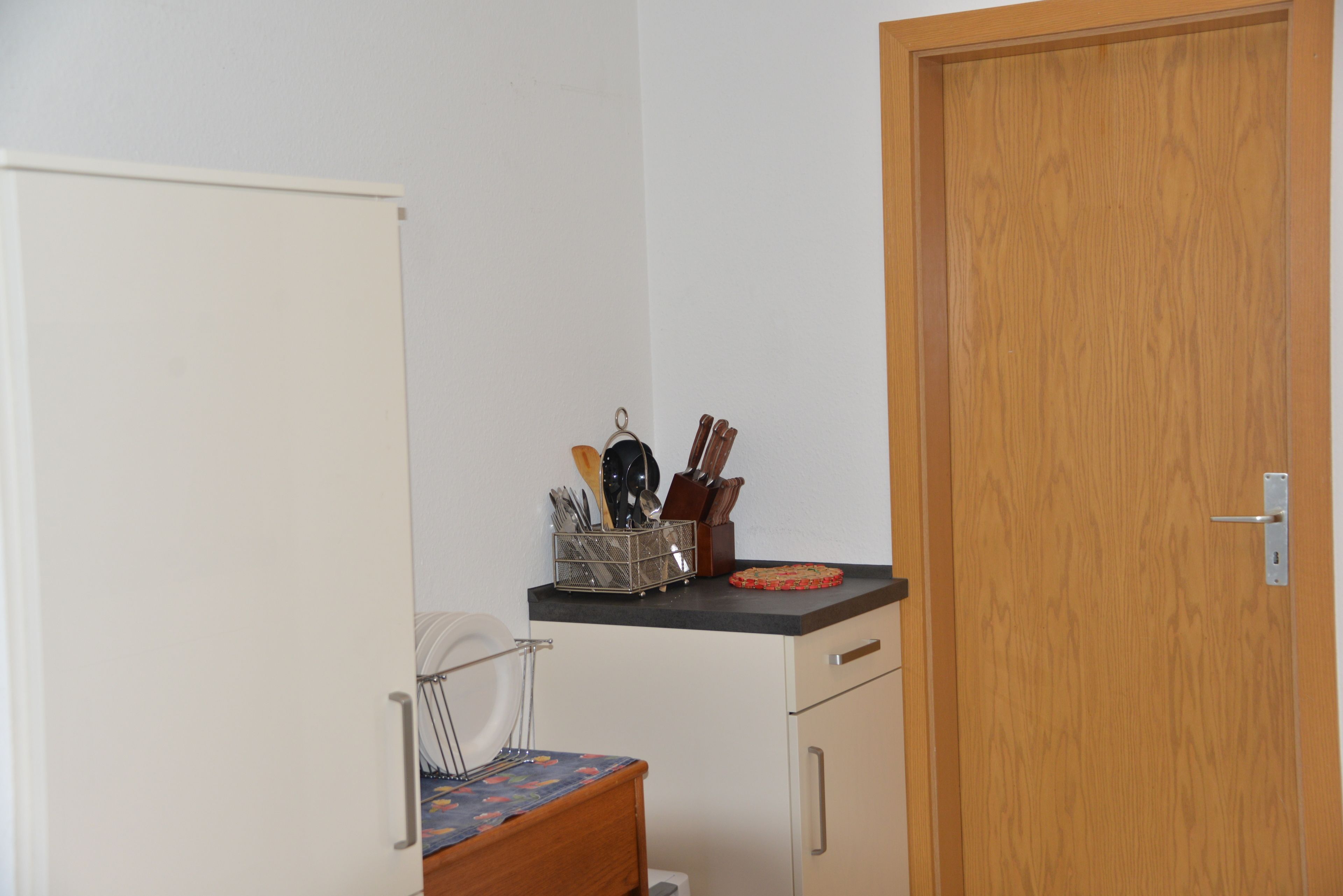 A small kitchen with a wooden door, a white cabinet, and a countertop with a knife holder and a small dish.
