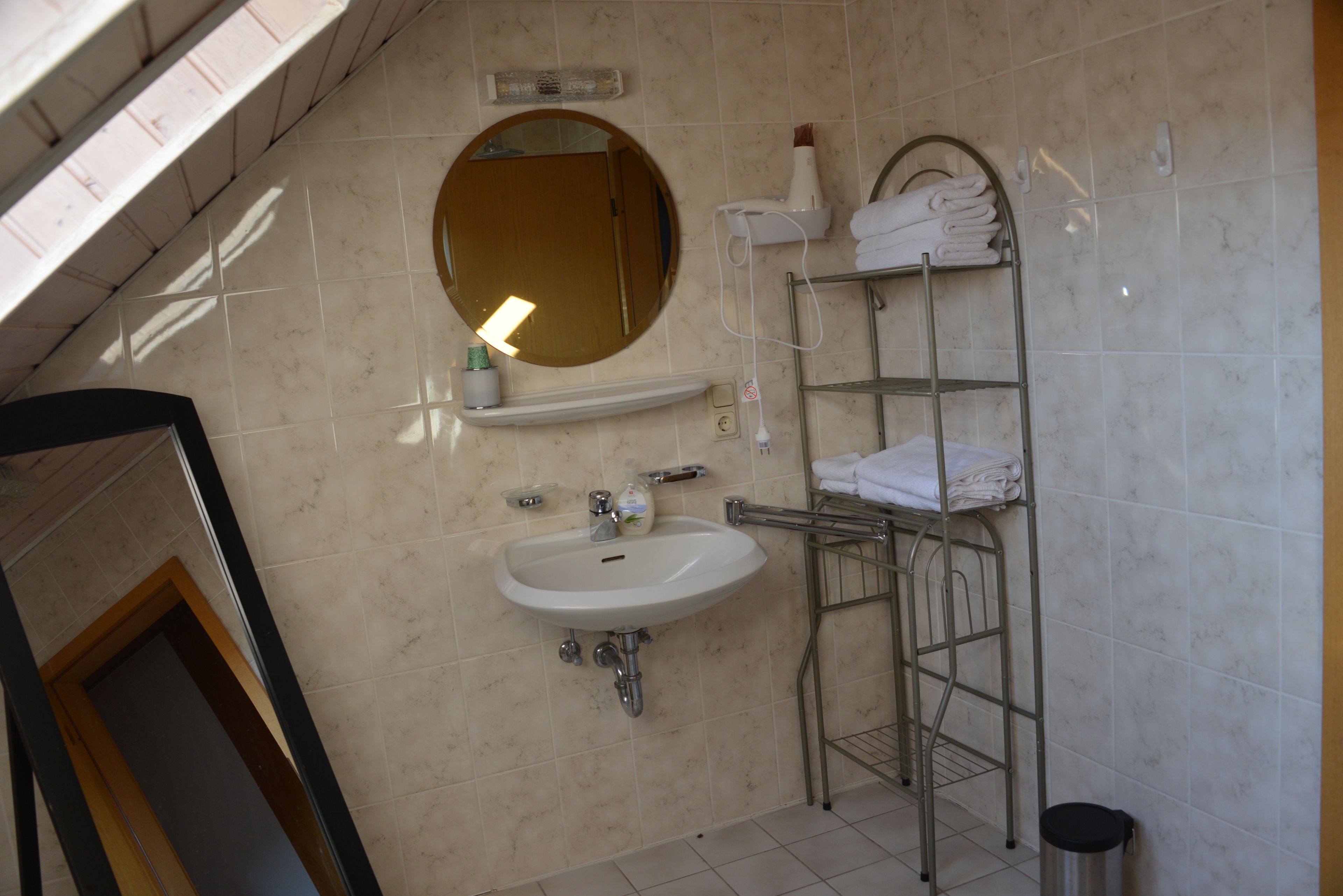 A bathroom with a sink, mirror, towel rack, and a trash can.
