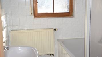 Une salle de bain avec une baignoire, des toilettes et une fenêtre.