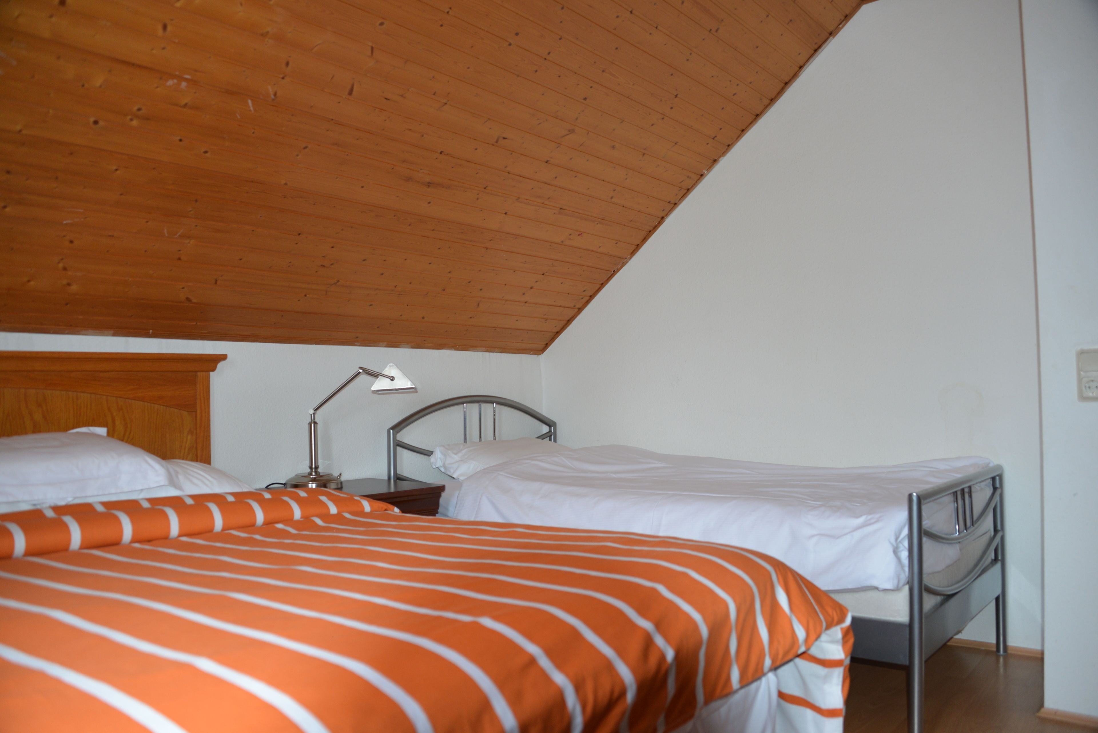 Un dormitorio con dos camas, techo de madera y paredes blancas.