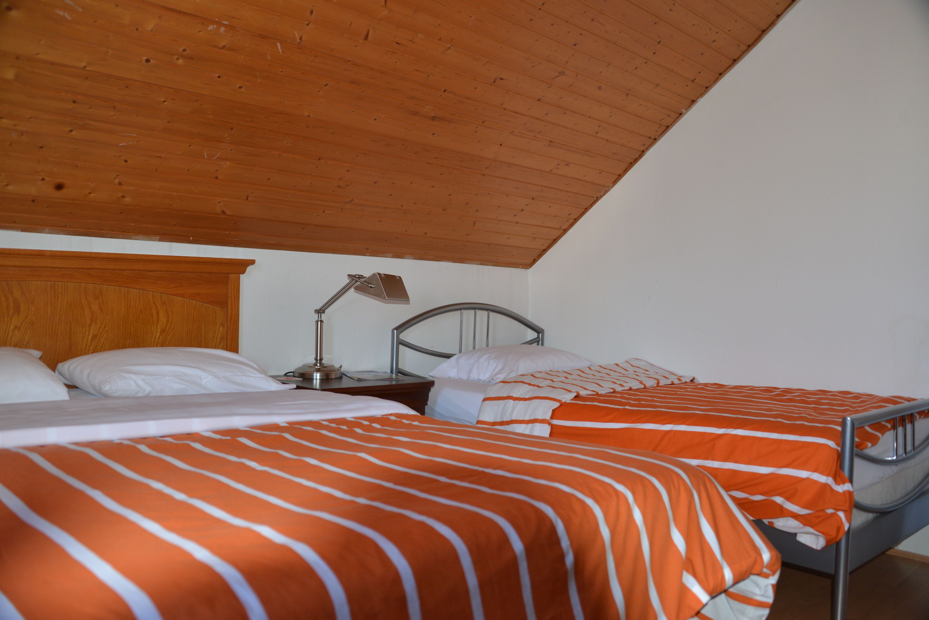 Quarto com duas camas, teto de madeira, paredes brancas e cabeceira de metal.