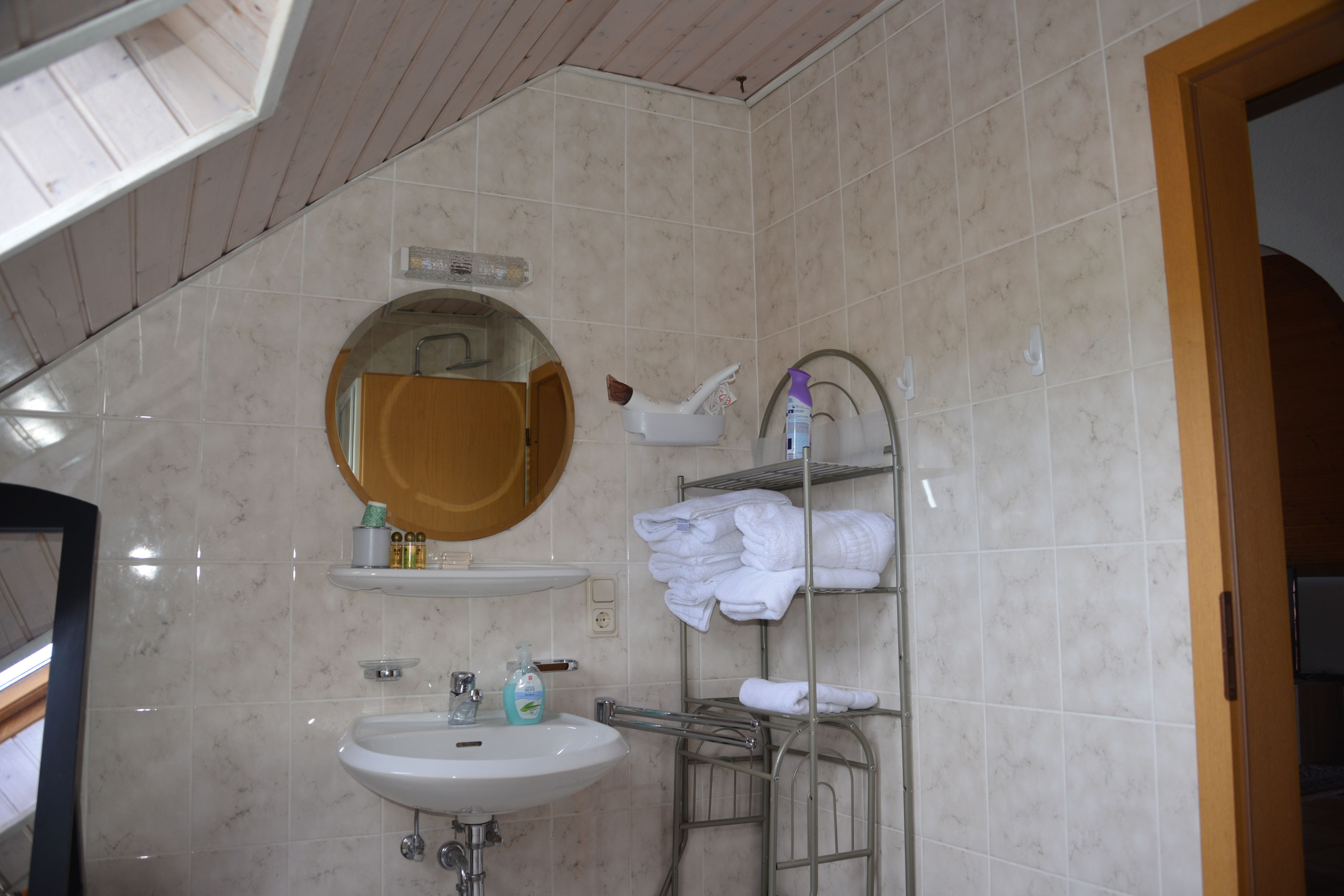 Un baño con lavamanos, espejo, toallero y artículos de aseo.