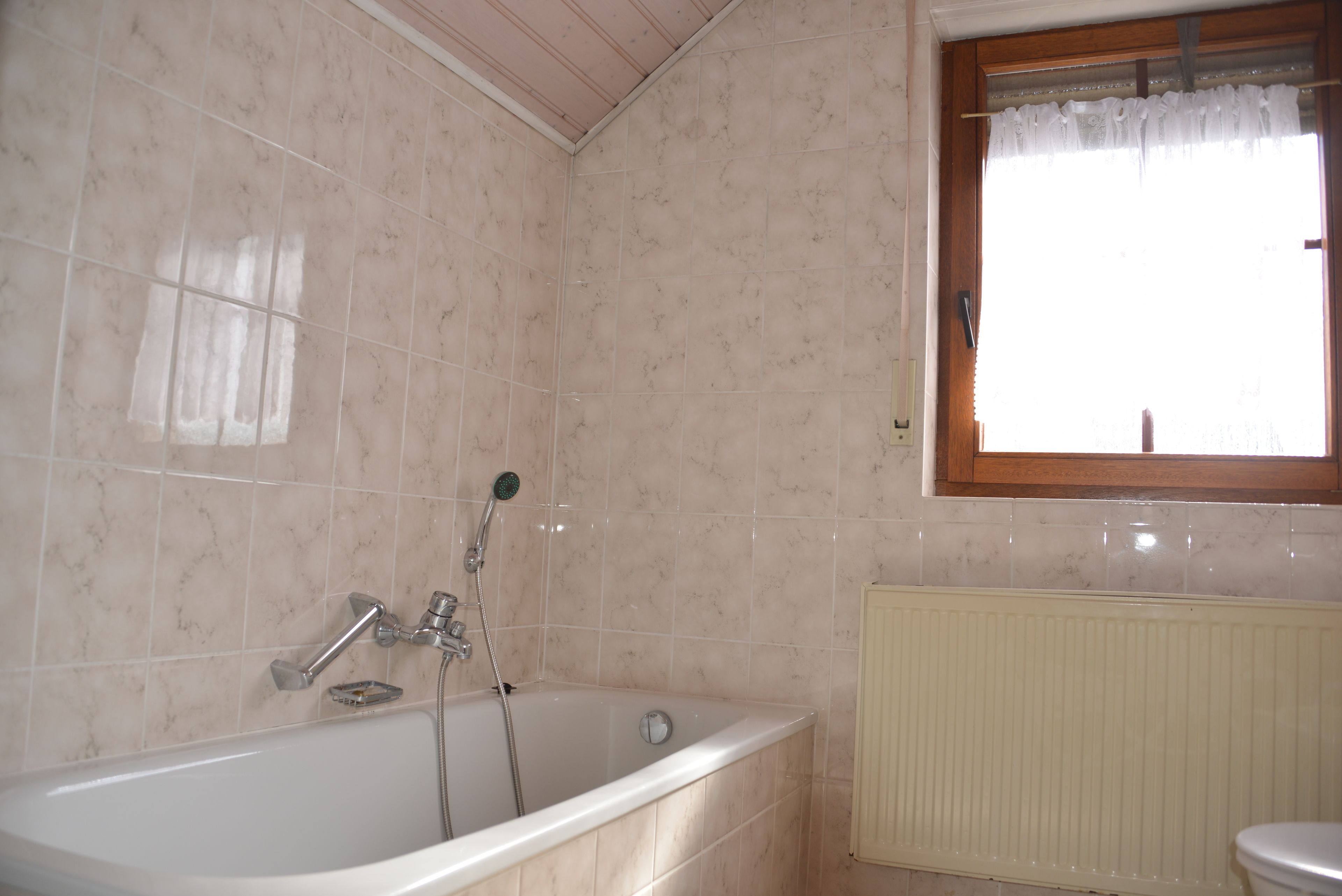 A bathroom with a bathtub, a window with a curtain, and a radiator.