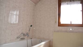A bathroom with a bathtub, a window with a curtain, and a radiator.