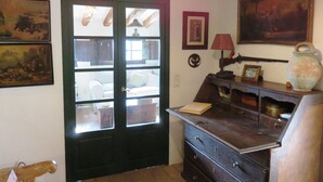 Una habitación con puerta de madera, un escritorio con cajones, una lámpara, un jarrón y cuadros en las paredes.