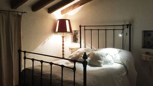 Un dormitorio con estructura metálica para la cama, una lámpara de noche y un ventanal con cortinas.
