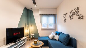 Ett modernt vardagsrum med en platt-TV, en blå soffa, ett litet runt bord och en dekorativ väggdekoration.