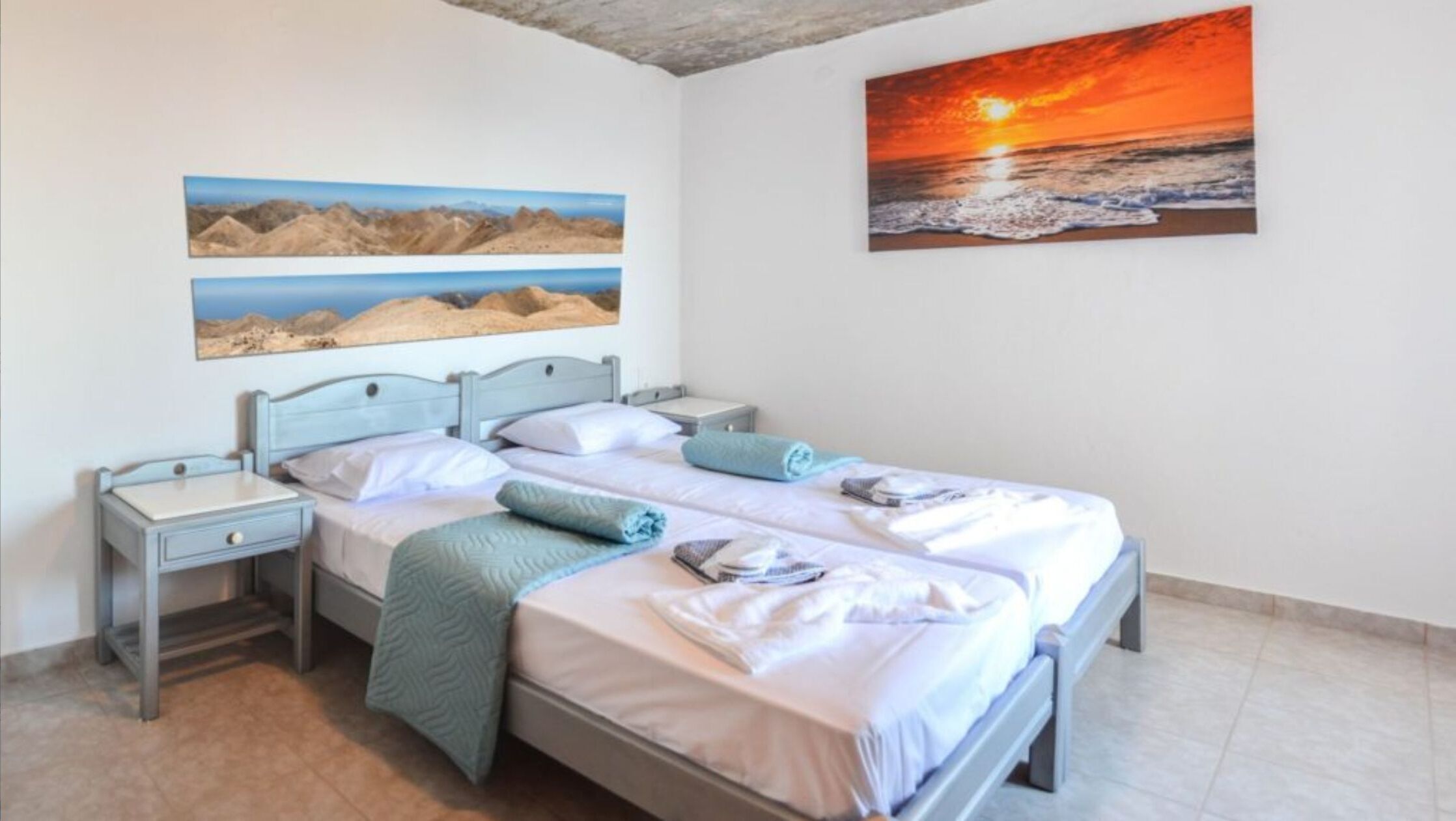 Een slaapkamer met een bed, twee nachtkastjes en een muur met drie schilderijen.