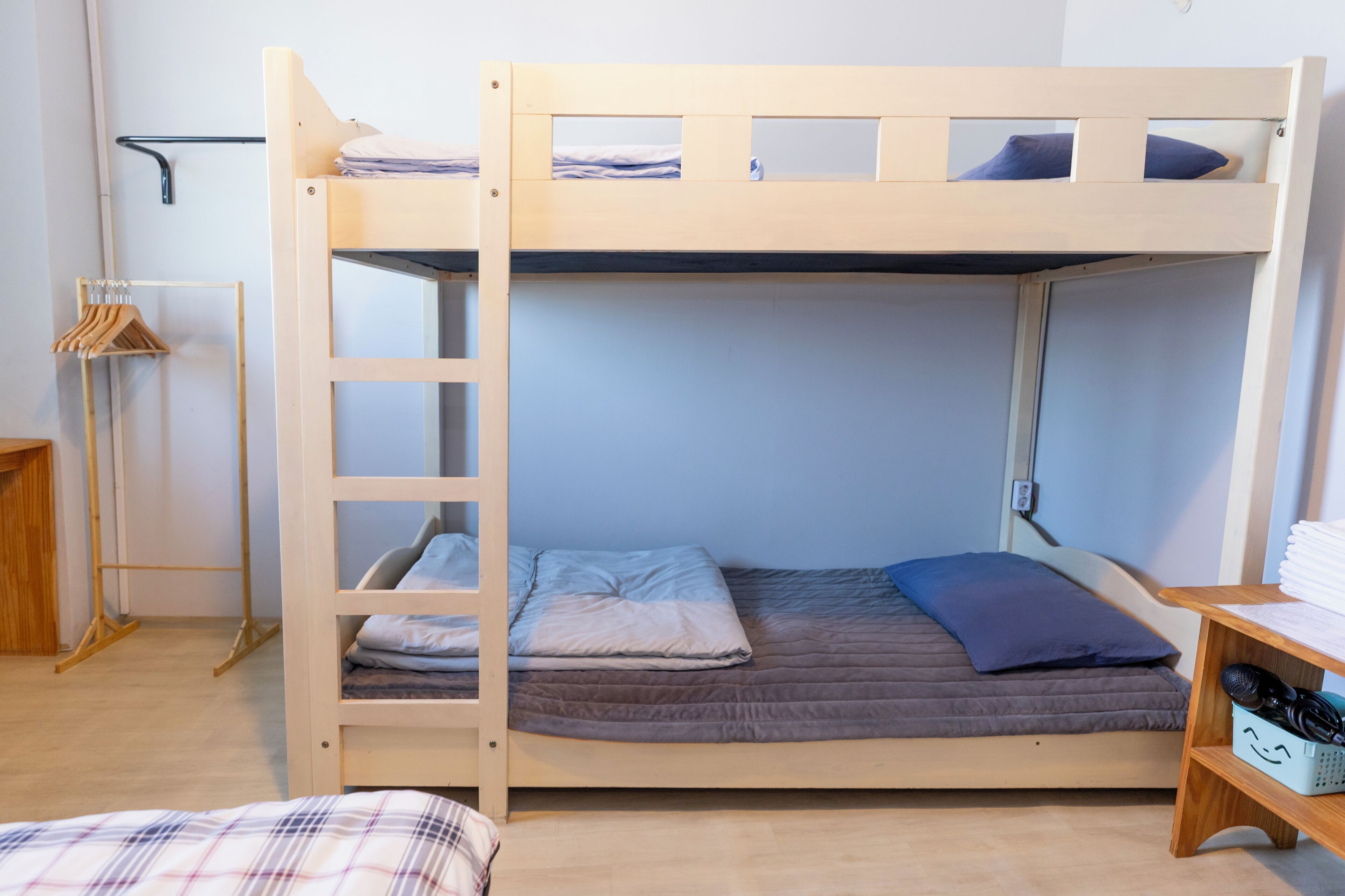 A bunk bed with a ladder, a bedside table, and a clothing rack.