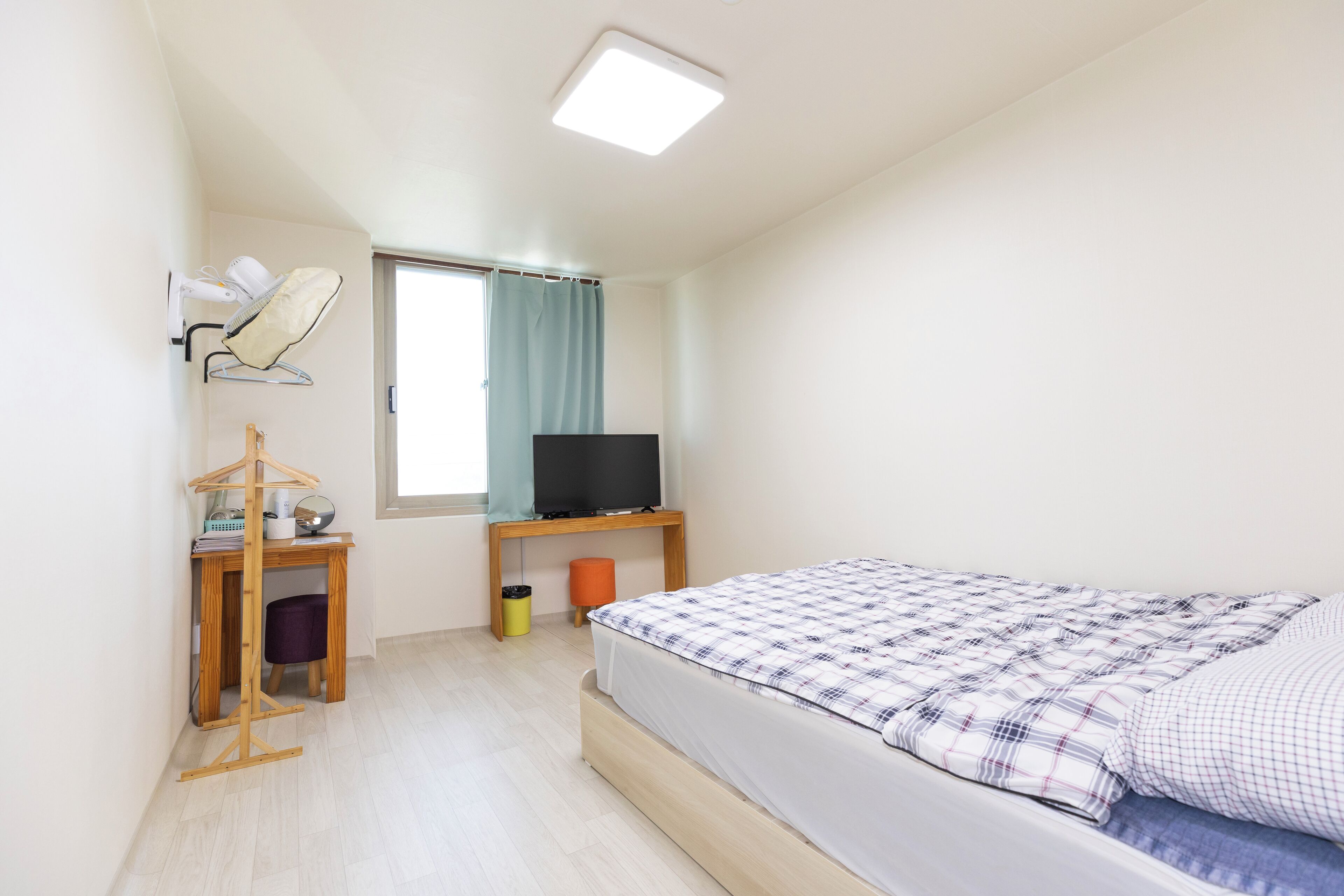 Une chambre à coucher avec un lit, un bureau, une chaise, une télévision et une fenêtre avec des rideaux.
