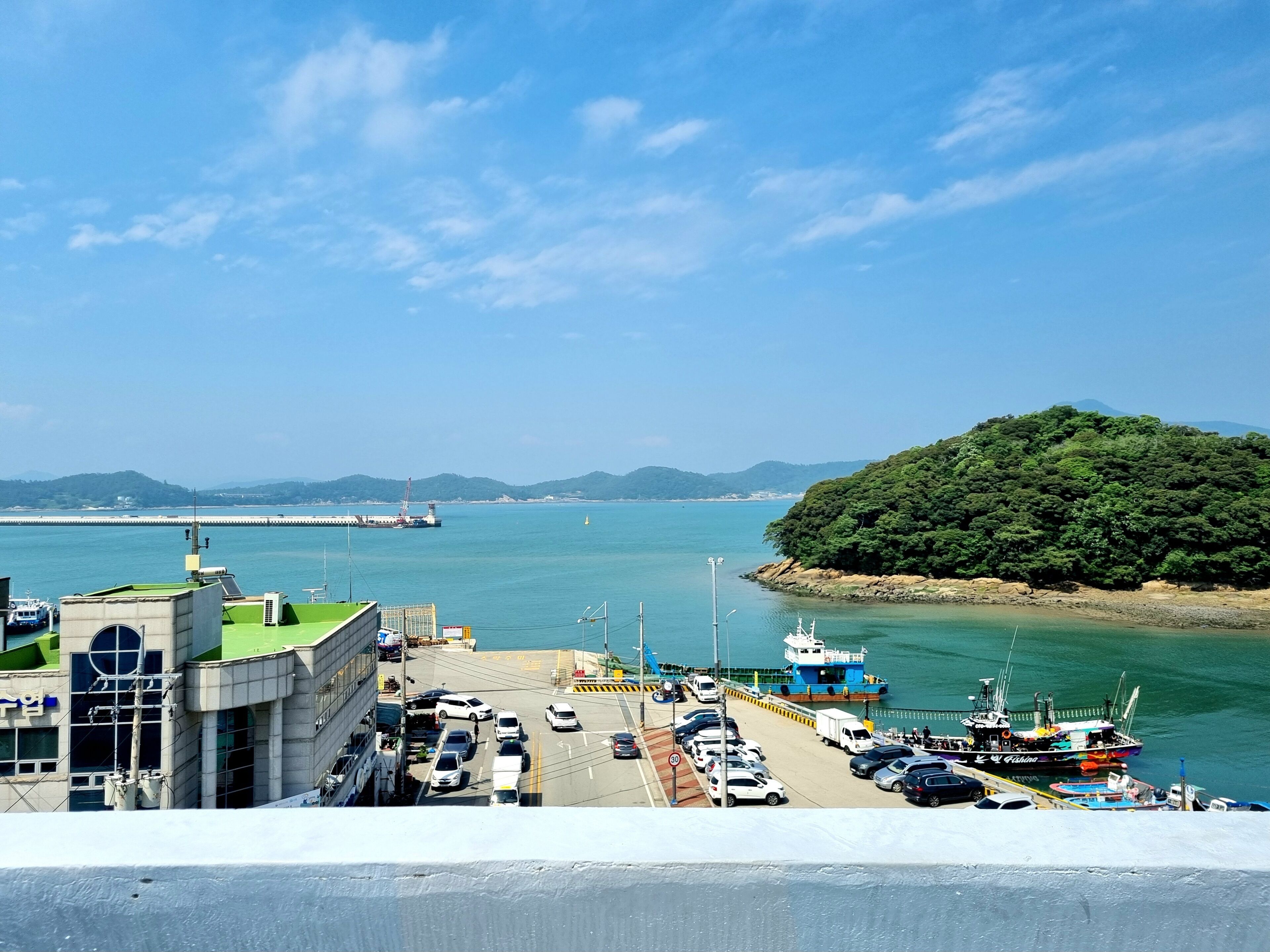 A coastal area with a parking lot, a bridge in the background, and a forested island.