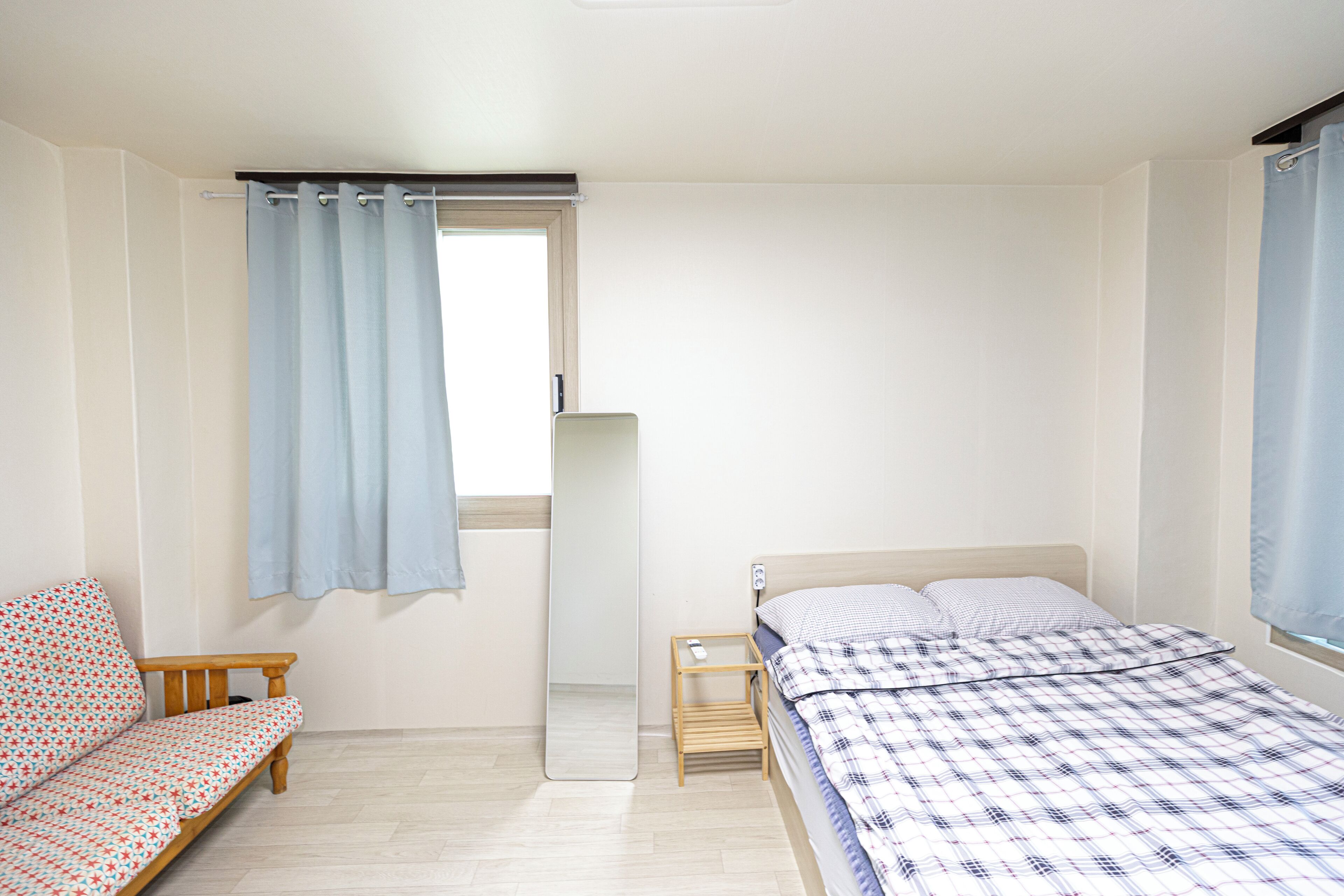 A bedroom with a bed, a small bedside table, a nightstand, a bench, and a mirror.