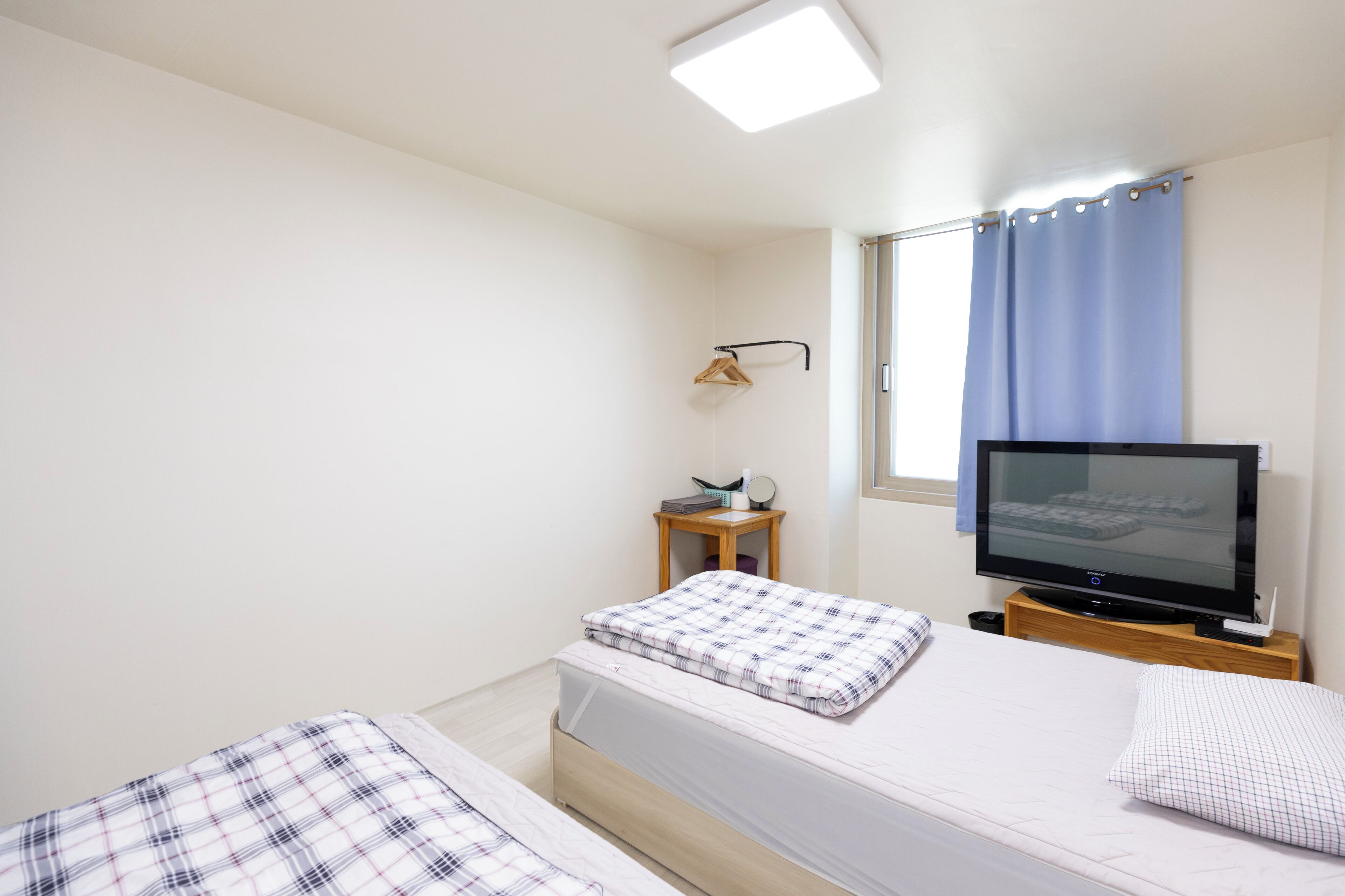Ein Schlafzimmer mit zwei Betten, einem Fernseher, einem kleinen Tisch mit Lampe und einem Fenster mit Vorhängen.