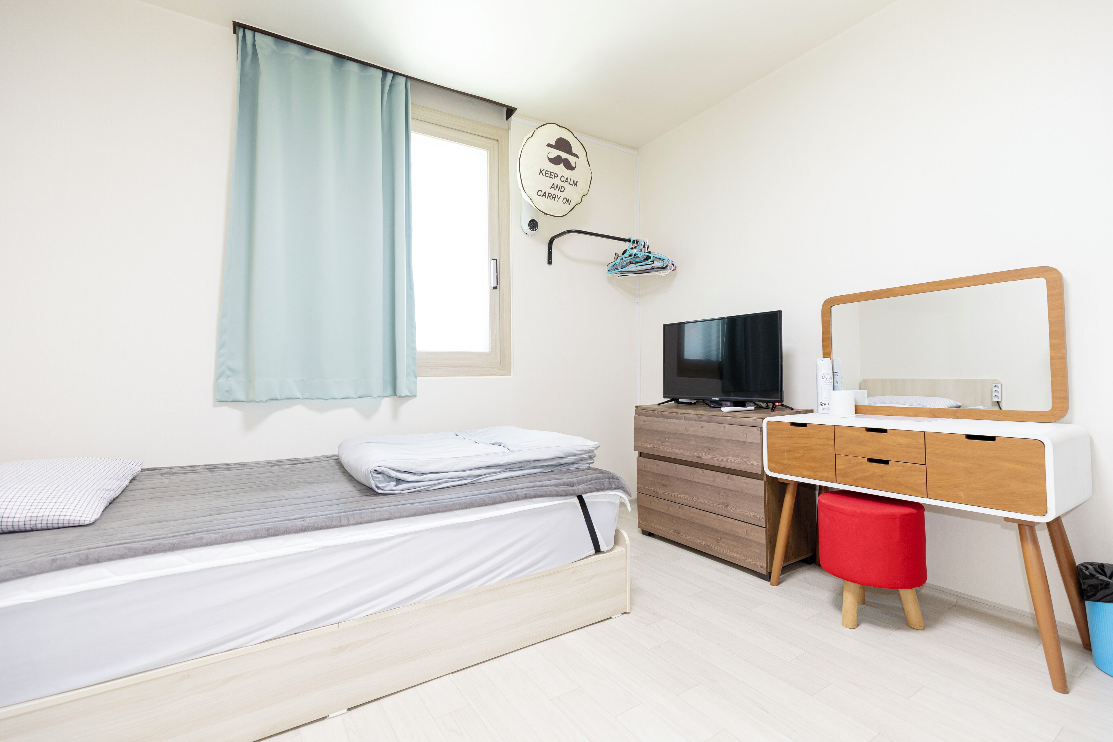 A bedroom with a bed, a dresser, a TV, and a mirror.