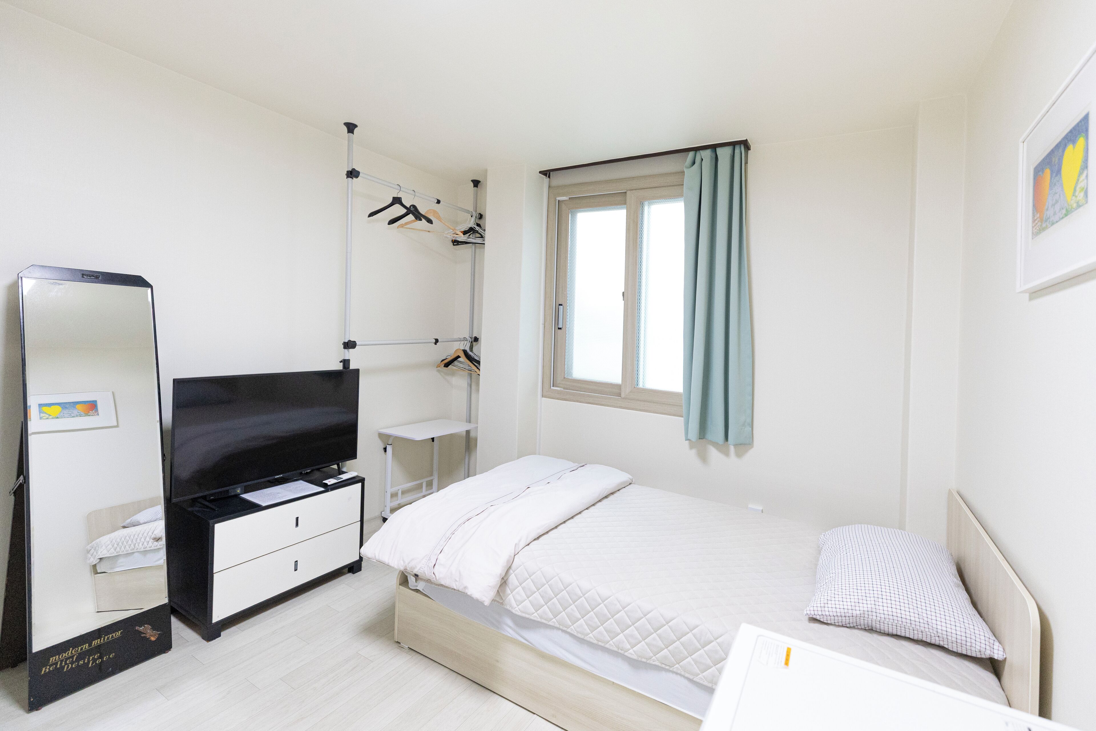 A bedroom with a bed, a dresser, a TV, a wardrobe, and a window with curtains.