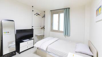 A bedroom with a bed, a dresser, a TV, a wardrobe, and a window with curtains.