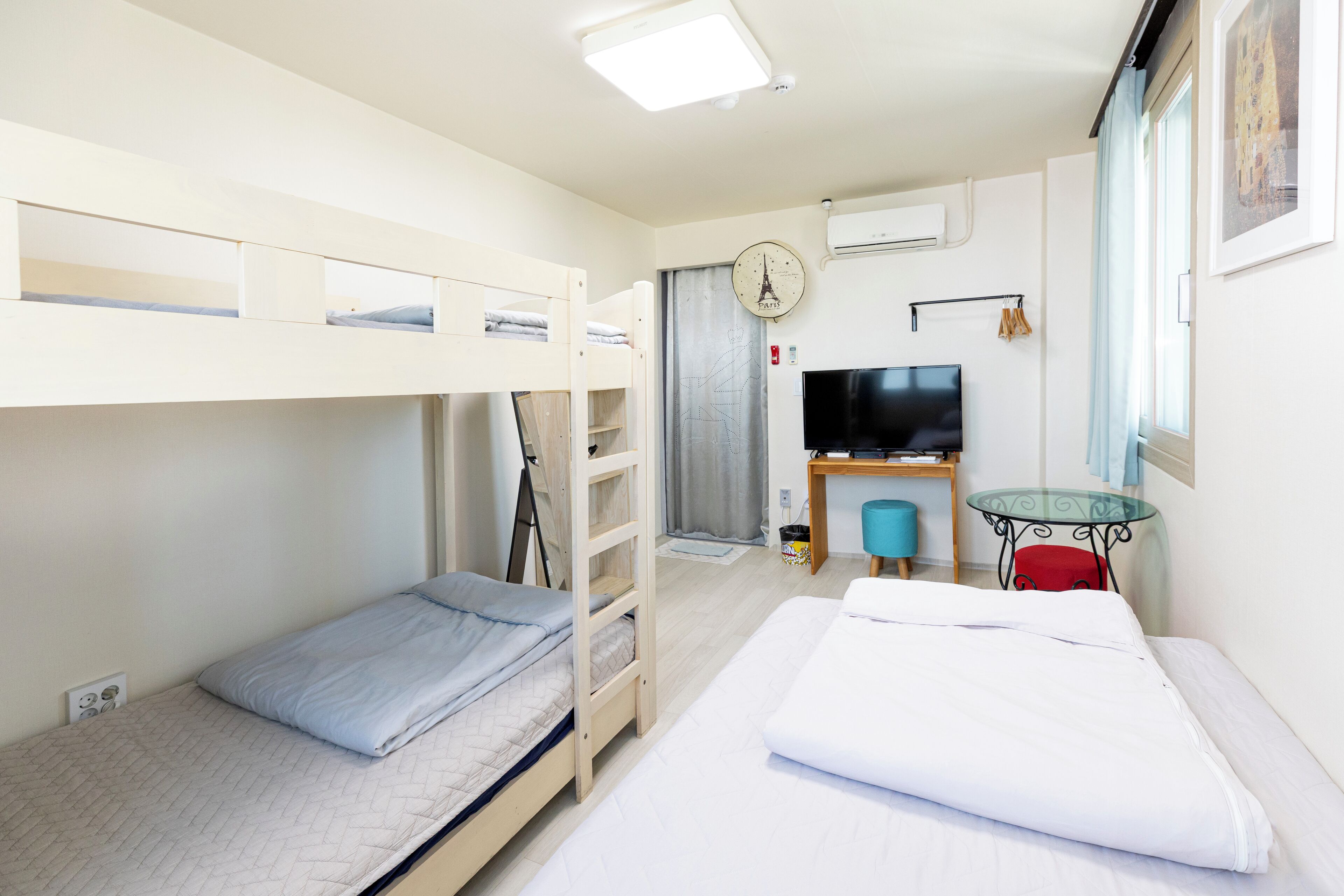 A room with bunk beds, a desk with a chair, a television, and a window with curtains.