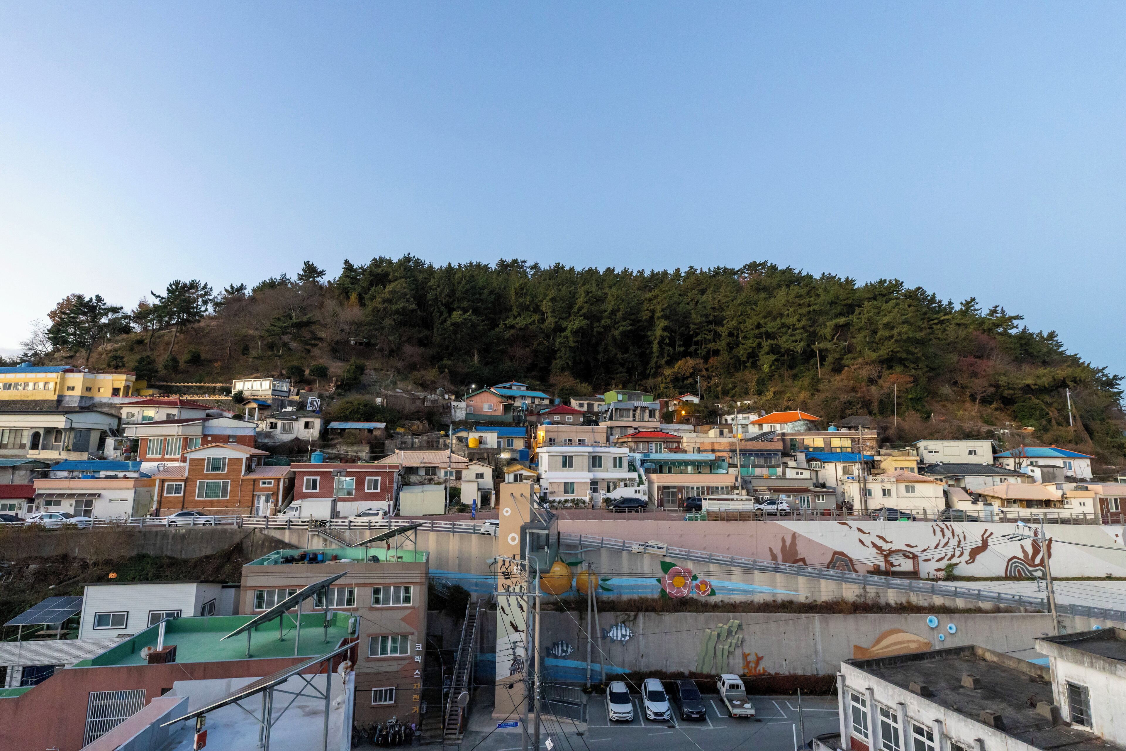 A residential area with houses on a hillside, a parking lot, and a mural on a building.
