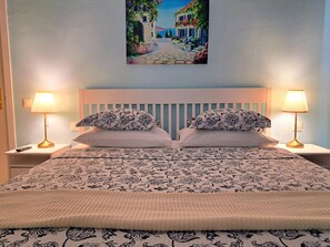 Cozy retreat with a neatly made bed, featuring a patterned bedspread and pillows, and a calming coastal scene above.