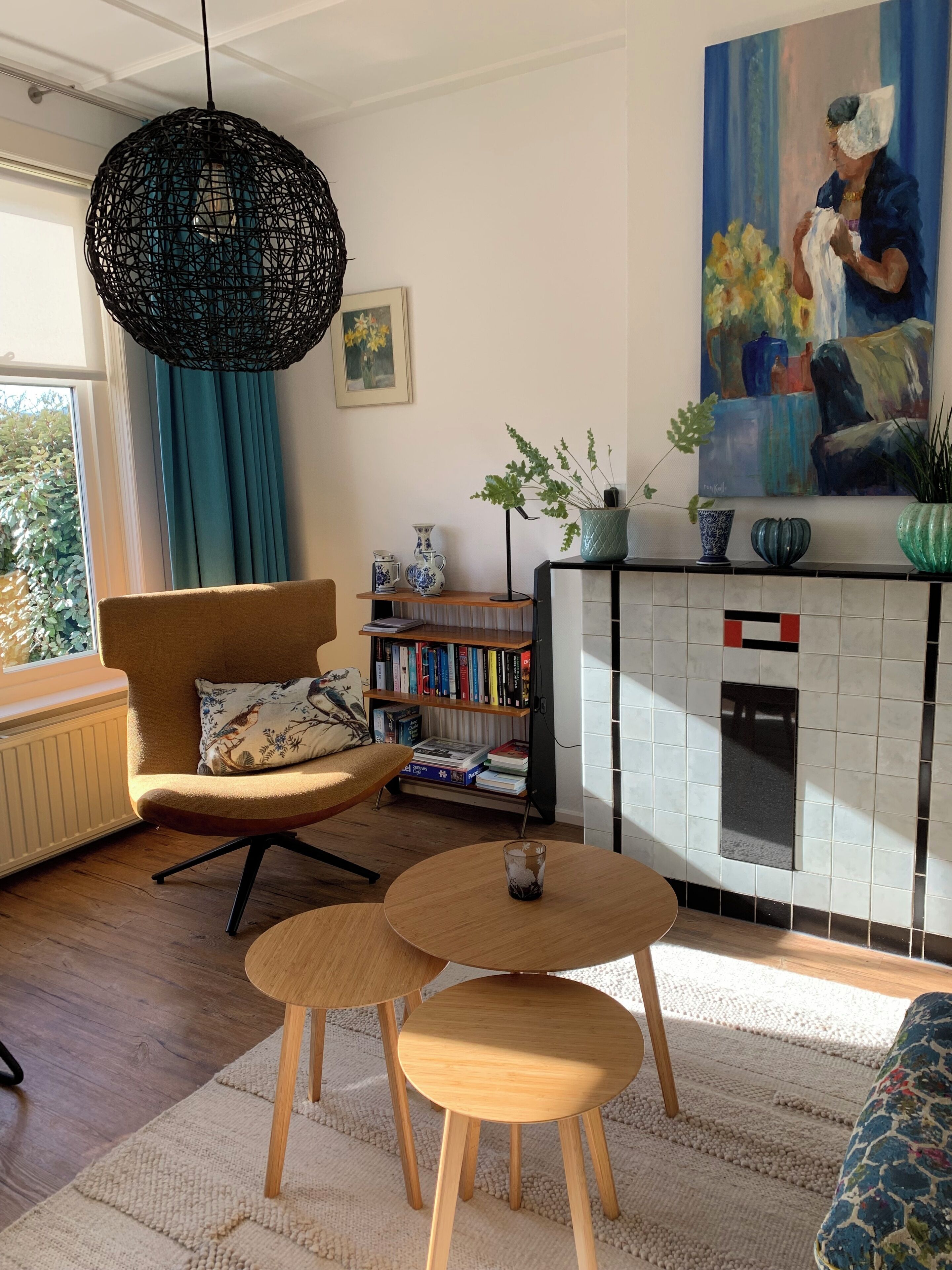 Un salon chaleureux avec un canapé, un fauteuil, une table ronde en bois, une bibliothèque, un tableau et un coin cuisine doté d’un mur recouvert de carreaux.