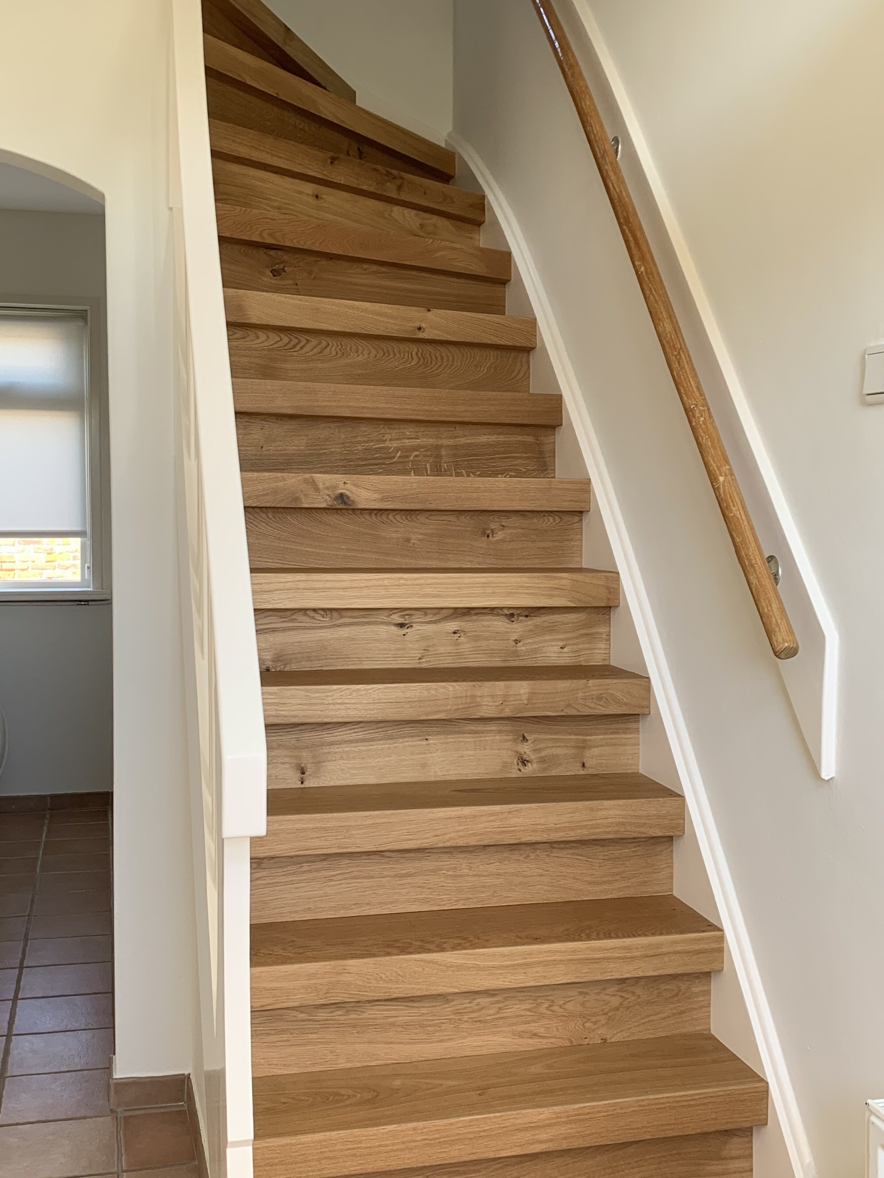 Un escalier en bois, avec des murs blancs et une main courante.