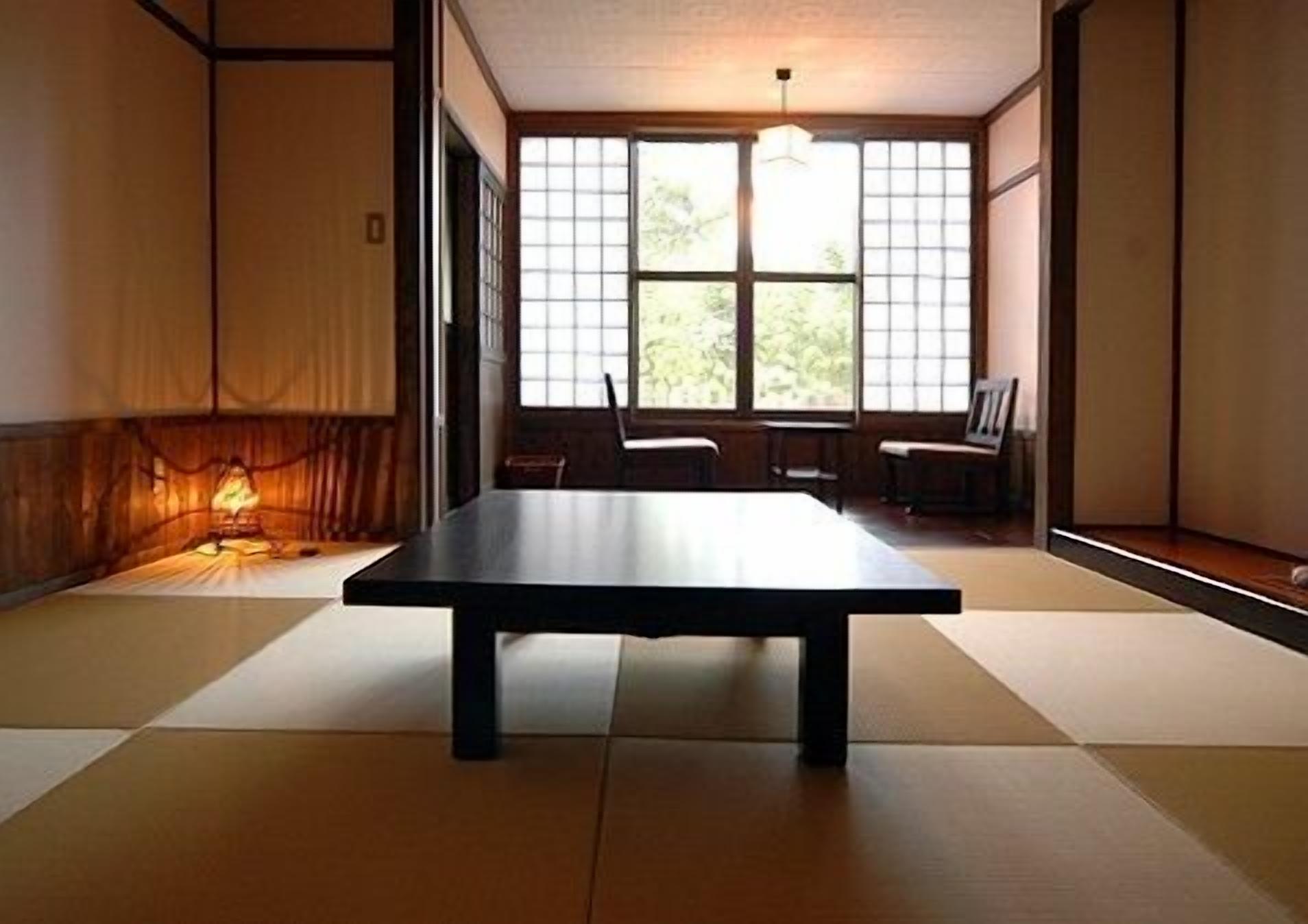 Ein Raum mit Tatami-Matten, einem niedrigen Tisch, Schiebetüren und einer hängenden Leuchte.