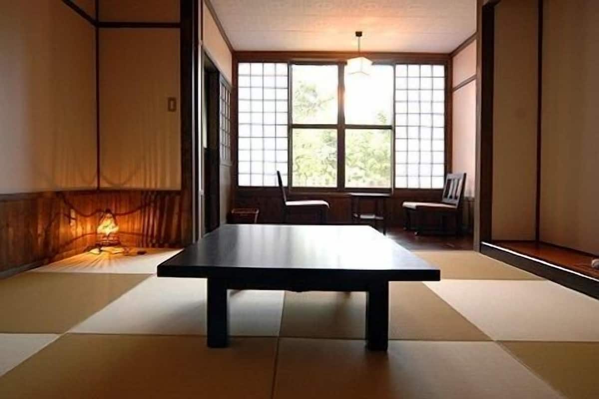Une pièce avec un sol recouvert de tatamis, une petite table basse, des portes coulissantes et un luminaire suspendu.