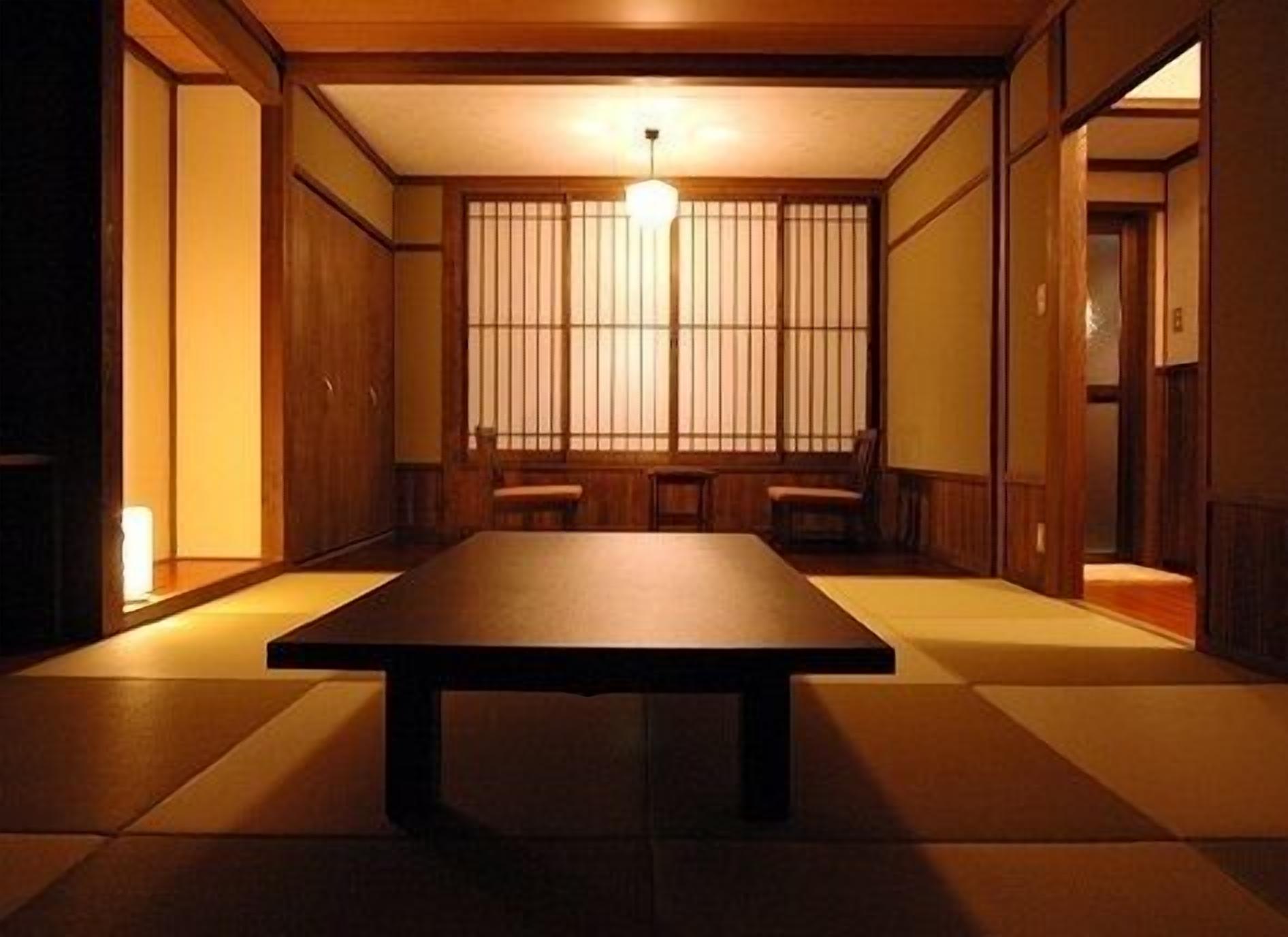 A traditional Japanese room with tatami flooring, a low table, sliding doors, and a hanging light fixture.